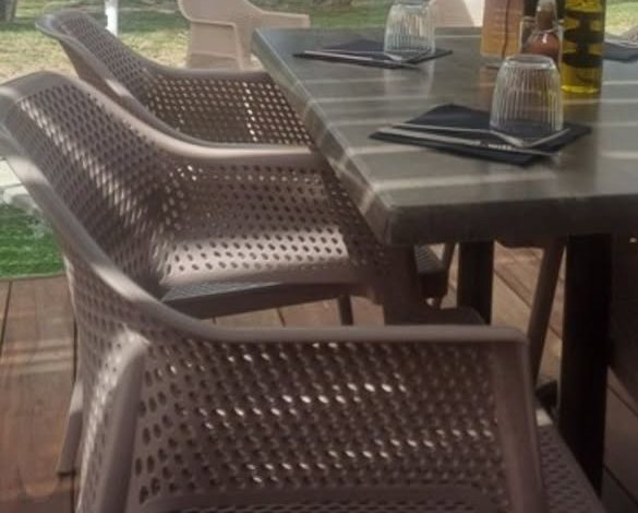 Une table dressée sur la terrasse de bois, sous les parasols, avec le lac derrière les arbres